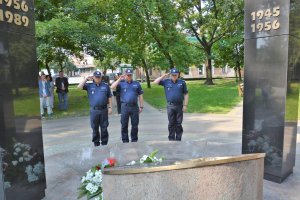 troje policjantów w granatowych mundurach oddają honor  pod pomnikiem