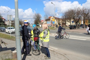 policjanci stoją na chodniku rozdają przechodniom odblaski. W tle jadą ulicą samochody