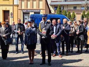 obchody rocznicy zbrodni katyńskiej policjantka składa kwiaty przed pomnikiem. stoi obok umundurowanego strażaka