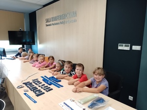 na zdjęciu widać dzieci siedzące przy biurku na sali konferencyjnej