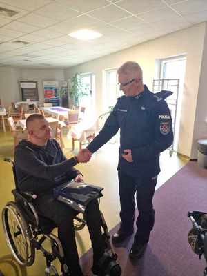 Komendant Wojewódzki Policji w Łodzi  podczas spotkania z policjantem w szpitalu. Komendant stoi policjant siedzi na wózku inwalidzkim.